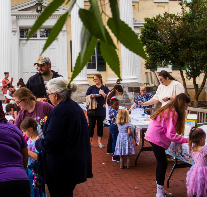 Elementary students, students, and teachers engaging in activities around a table on the McMurran lawn.