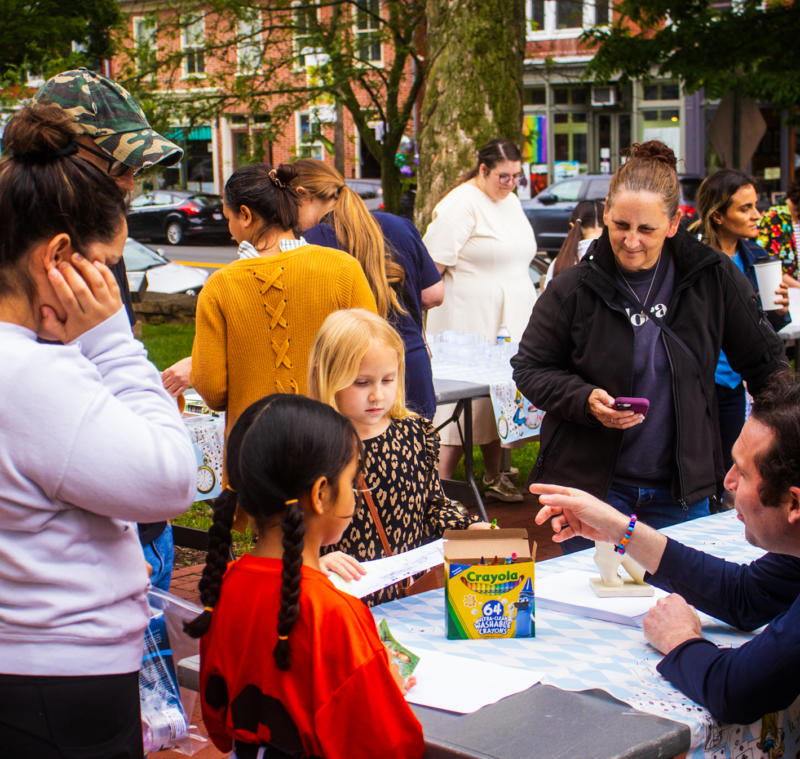 Elementary students, students, and teachers engaging in activities around a table on the McMurran lawn.