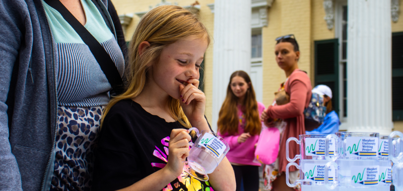 Elementary students, students, and teachers engaging in activities around a table on the McMurran lawn.